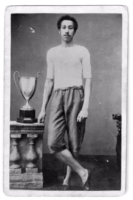 black and white image of Arthur Wharton, standing cross legged next to a trophy